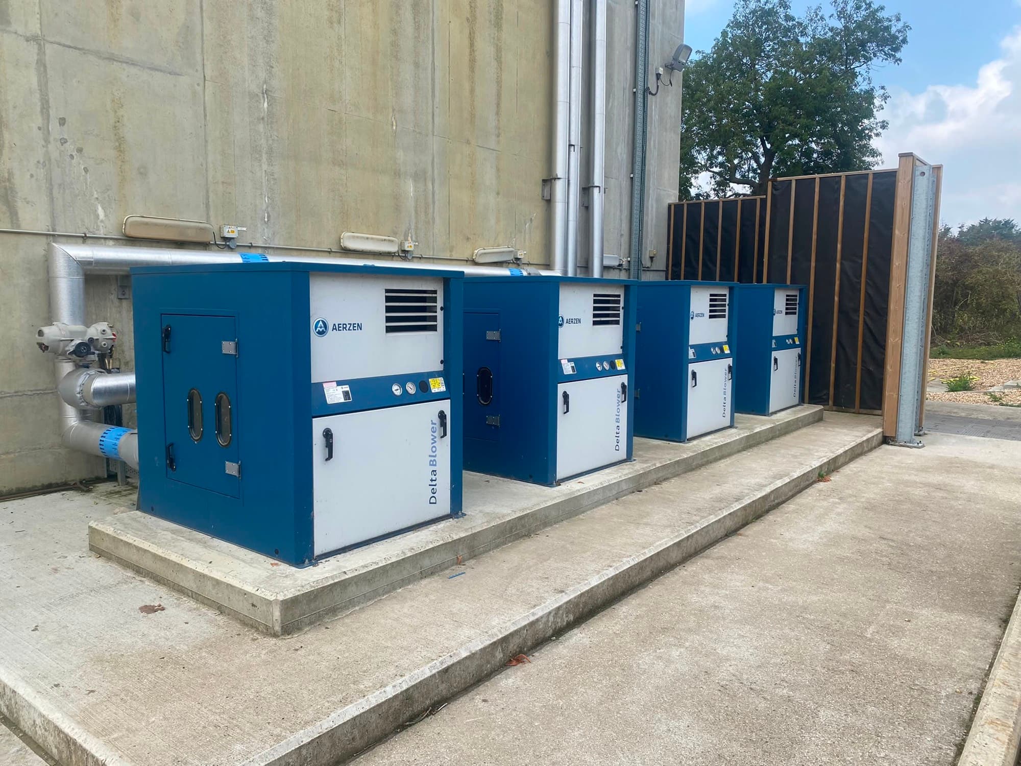Four Aerzen Delta blower packages on a concrete plinth outside a farm silo, timber acoustic fence behind