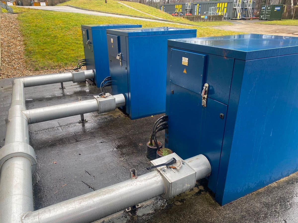 Three dark blue acoustic enclosures with galvanised discharge pipework