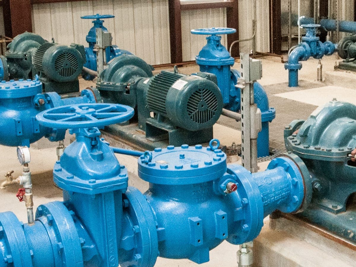 Blue flanged swing check valve with a bolted cover, fitted between a gate valve and a split-case pump