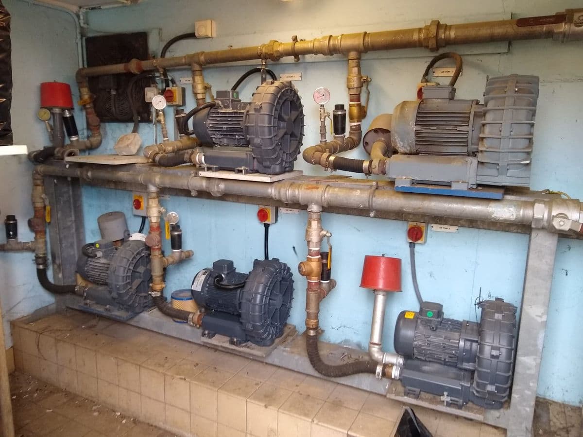 Six side-channel blowers mounted on a two-tier wall frame with brass pipework
