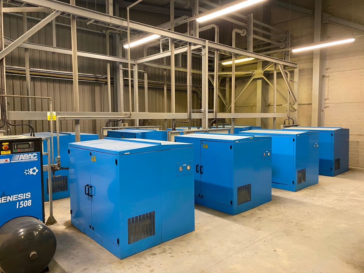 Plant room with rows of blue acoustic blower enclosures beneath a steel gantry