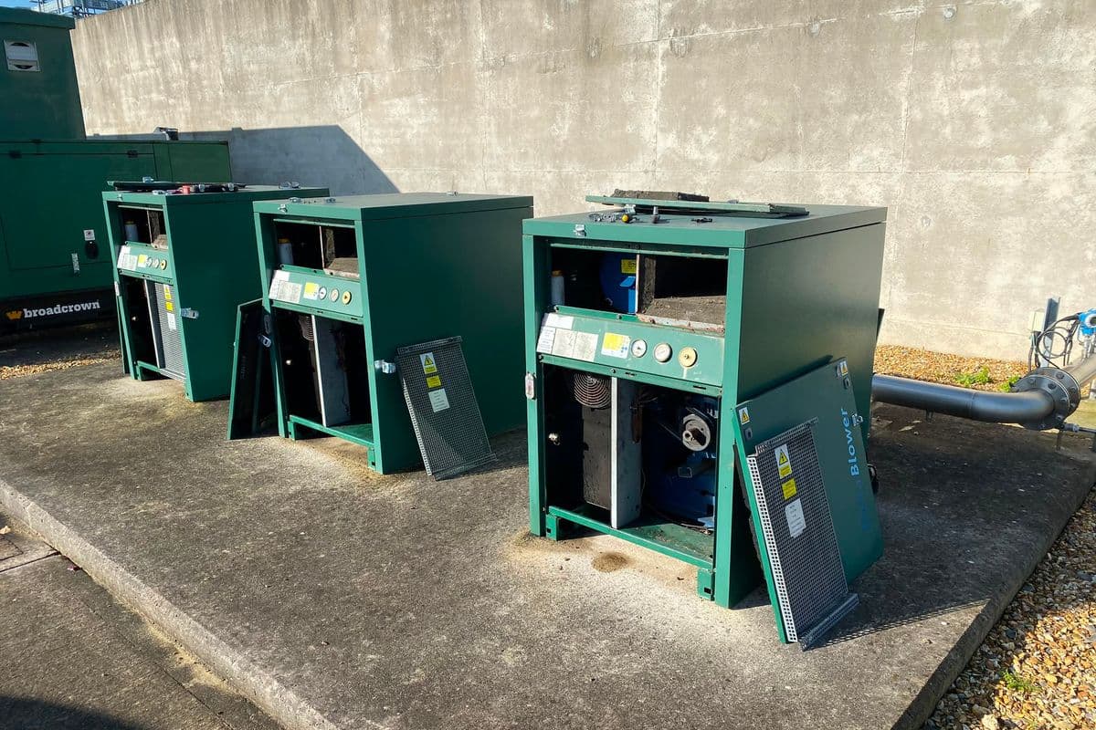 Three green blower enclosures with side panels off and internals exposed on a concrete plinth