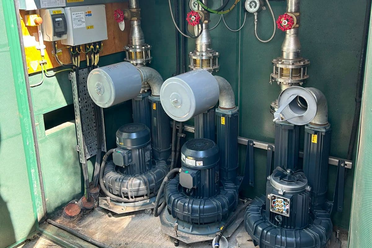 Three side-channel blowers under service inside an opened green kiosk