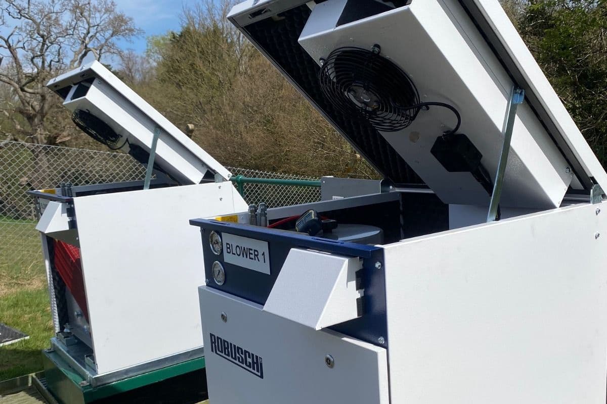Two Robuschi Robox enclosures with their lids raised for servicing on a green skid